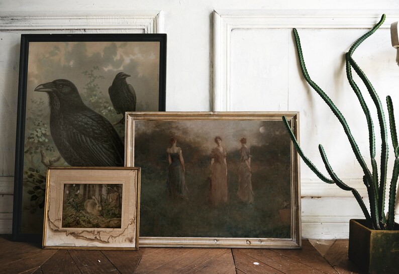 May include: Three framed paintings on a white wall with a green plant in a pot. The paintings are all different sizes and have different subjects. The first painting is of two crows, the second is of three women in a field, and the third is of a rabbit in a forest.