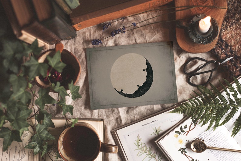Puede incluir: Una impresi&oacute;n de estilo vintage de una luna creciente con un dise&ntilde;o verde oscuro y negro sobre un fondo gris claro. La impresi&oacute;n est&aacute; sobre una mesa con libros, plantas y otros art&iacute;culos decorativos.