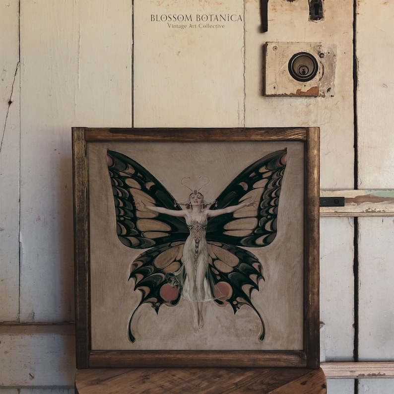 May include: A framed vintage art print featuring a woman with butterfly wings. The woman is wearing a white dress and has her arms outstretched. The butterfly wings are black, green, and yellow.