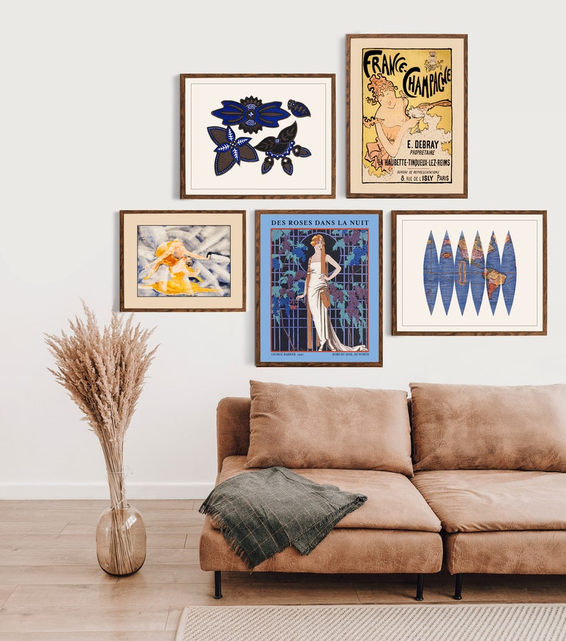 Puede incluir: Una colecci&oacute;n de impresiones art&iacute;sticas enmarcadas exhibidas en una pared blanca sobre un sof&aacute; marr&oacute;n. Las impresiones presentan anuncios vintage y dise&ntilde;os abstractos en varios colores, incluyendo azul, amarillo y beige. Un jarr&oacute;n de hierba de la pampa seca est&aacute; en el suelo.