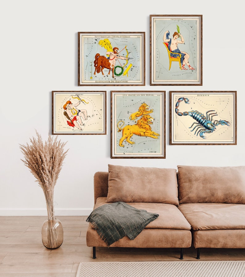 May include: Five framed vintage constellation prints. The prints feature colourful illustrations of zodiac signs like Sagittarius, Capricorn, Gemini, Leo, and Scorpio. The prints are displayed on a white wall above a brown sofa with a green blanket.
