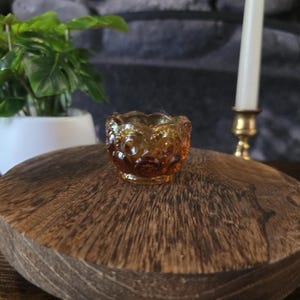 Könnte beinhalten: Eine kleine bernsteinfarbene Glasschale mit einem sich wiederholenden Mond- und Sternmuster, das auf der Außenseite eingeprägt ist. Die Schale hat einen gewellten Rand und einen runden Boden aus durchscheinendem Pressglas.