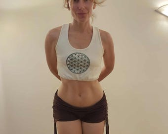May include: A white crop top with a green geometric design and brown shorts with drawstring details. The outfit is suitable for yoga or other fitness activities.