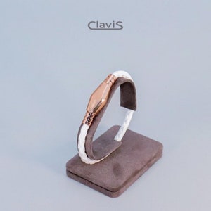 Könnte beinhalten: Weißes Lederarmband mit einem roségoldenen Verschluss und dem Wort "Clavis" auf dem Verschluss eingraviert.