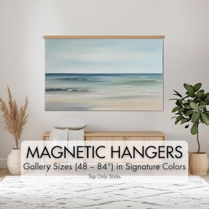 May include: A framed landscape painting of the ocean in shades of blue, green, and beige, displayed with a wooden magnetic hanger. The text "MAGNETIC HANGERS" and "Gallery Sizes (48 - 84") in Signature Colors" is visible.