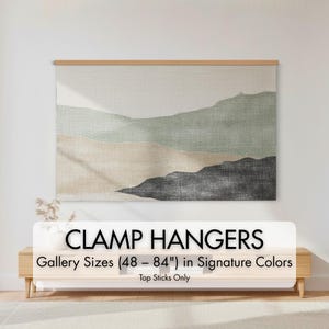 May include: A landscape art print with a mountain design in shades of green, beige, and black, displayed with a wooden clamp hanger. The text "CLAMP HANGERS" and "Gallery Sizes (48 - 84") in Signature Colors" is visible.