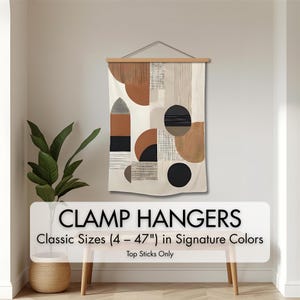 May include: A canvas wall hanging with a geometric design in shades of brown, black, and cream, suspended from a wooden clamp hanger. The text "CLAMP HANGERS" and "Classic Sizes (4 - 47") in Signature Colors" is displayed.