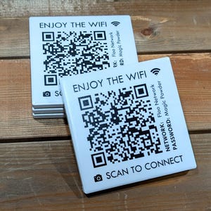 May include: White square cards with the text "ENJOY THE WIFI" and a QR code. The cards also have the text "SCAN TO CONNECT" and network information. The cards are stacked on a wooden surface.