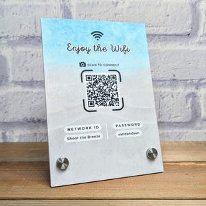 May include: A blue and white sign with the text "Enjoy the Wifi" and a QR code. The sign also includes the network ID "Shoot the Breeze" and the password "sandandsun".