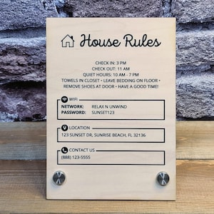 May include: A wooden sign with the words "House Rules" and a house icon. The sign includes check-in/out times, quiet hours, and other rules. It also displays Wi-Fi network and password, location, and contact information.