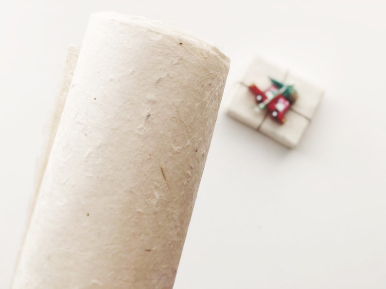 Puede incluir: Un rollo de papel de regalo blanco texturizado con un aspecto de fibra natural. El papel est&aacute; enrollado y listo para ser utilizado para envolver regalos.