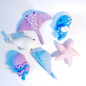 May include: A set of crocheted sea creatures, including a stingray, a dolphin, a jellyfish, a starfish, and a seahorse. The creatures are all made in different colors, including pink, blue, and white.