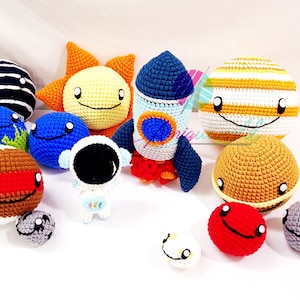 May include: A set of crocheted planets and a rocket, including a yellow sun, a blue planet with green continents, a brown planet with a red stripe, a grey planet, a striped yellow planet, a black and white striped planet, a blue planet, a grey planet, a red planet, a white planet, and a white astronaut.