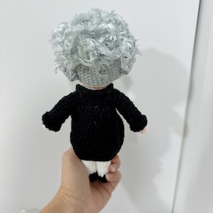 May include: A crocheted doll with gray curly hair, wearing a black sweater and white pants.
