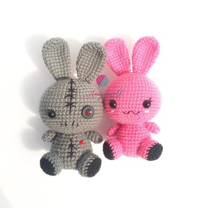 May include: Two crocheted bunny plushies, one grey with a button eye and stitched details, the other pink with embroidered eyes and a sweet expression.