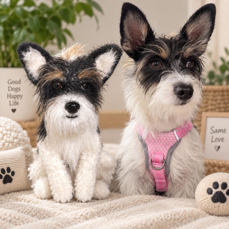 May include: A plush dog figurine with black, white, and tan fur sits beside a small dog wearing a pink mesh harness. The plush features a black nose and dark eyes. The live dog has upright ears and a white chest. Text reads Good Dogs Happy Life.