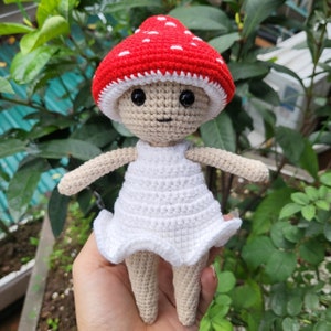 May include: A crocheted doll wearing a red and white mushroom hat and a white dress.