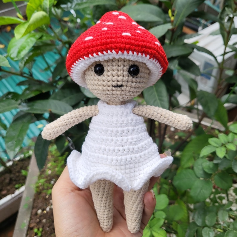 May include: A crocheted doll wearing a red and white mushroom hat and a white dress.