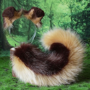 Pode incluir: Um conjunto de orelhas de animais de pele sint&eacute;tica castanha e bege numa bandolete e uma cauda a condizer. A cauda &eacute; uma mistura de pele castanha, bege e creme. Os artigos s&atilde;o exibidos numa superf&iacute;cie verde com um fundo de floresta.