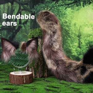 May include: A set of faux fur animal ears on a clear headband and a long, matching faux fur tail. The ears are brown, black, and tan with a pointed shape. The text "Bendable ears" is visible. The tail is long, thick, and multi-colored.