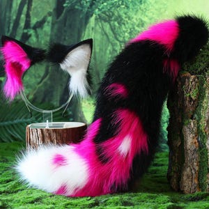 Può includere: Un set di accessori cosplay con una coda e orecchie da volpe nere, bianche e rosa. La coda è prevalentemente nera con accenti rosa e bianchi. Le orecchie sono nere con dettagli interni rosa e bianchi, attaccate a una fascia trasparente.