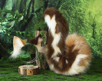 May include: A brown, white, and tan faux fur tail and matching ear headband set. The tail is curled and fluffy, with a white stripe down the back. The ears are attached to a clear headband.