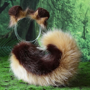 Pode incluir: Um conjunto de cauda e faixa de cabelo em pele sint&eacute;tica castanha, bege e branca. A cauda &eacute; encaracolada e fofa, e a faixa de cabelo apresenta pequenas orelhas arredondadas. O conjunto foi concebido para se assemelhar a um animal.