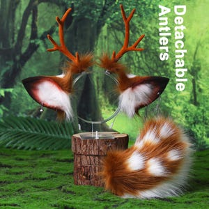 Puede incluir: Un conjunto de orejas y astas de ciervo de piel sintética con el texto Detachable Antlers, con pelaje marrón y blanco, astas naranjas y pequeñas campanas plateadas en las orejas, junto a una cola de piel sintética marrón y blanca a juego.