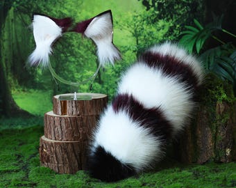 Può includere: Un set cosplay in finta pelliccia con una fascia per capelli con orecchie bianche e bordeaux e una coda abbinata. La coda è principalmente bianca con accenti bordeaux e neri.