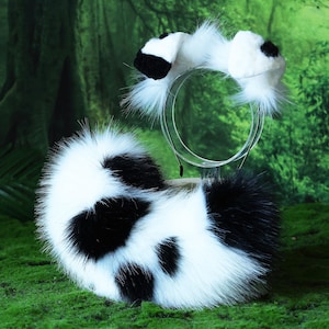 Puede incluir: Una cola de piel sintética en blanco y negro y una diadema a juego con orejas. La cola es redonda y esponjosa con manchas negras. La diadema tiene orejas blancas con puntas negras. Los artículos se exhiben sobre musgo verde.