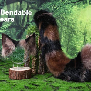 May include: A set of faux fur animal ears on a headband and a matching long faux fur tail. The ears are brown, black, and tan with a pointed shape and the text Bendable ears. The tail features a striped pattern of black, brown, and tan fur.