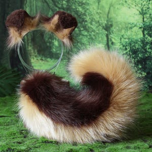 May include: A brown and tan faux fur tail and matching ear headband set. The tail is a fluffy, rounded shape with a dark brown center and lighter tan edges. The headband has two small, matching ears.