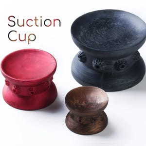 Peut inclure: Trois ventouses de différentes couleurs et matières. Une ventouse rouge, une ventouse noire et une ventouse en bois brun.