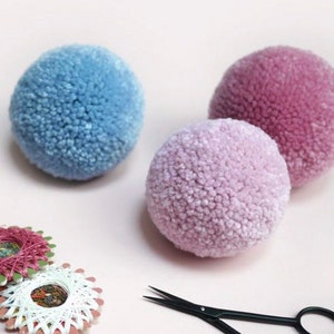 May include: Three fluffy pom poms in shades of blue and pink. The pom poms are made of yarn and are perfect for crafting projects.
