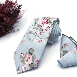 Könnte beinhalten: Eine hellblaue Krawatte mit einem Blumenmuster mit rosa und weißen Blüten. Die Krawatte wird mit einem passenden Einstecktuch geliefert.