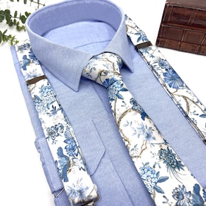 Könnte beinhalten: Eine weiße und blaue Krawatte mit floralem Muster und Hosenträger. Die Krawatte hat einen weißen Hintergrund mit blauen floralen Mustern. Die Hosenträger haben einen weißen Hintergrund mit blauen floralen Mustern. Die Hosenträger sind an einem hellblauen Hemd mit Knöpfen befestigt.