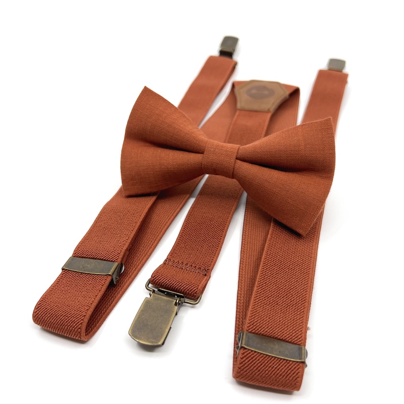 Op de afbeelding: Een set van oranje bretels en een bijpassende strik. De bretels hebben verstelbare banden en metalen clips. De strik is gemaakt van een zachte, gestructureerde stof.