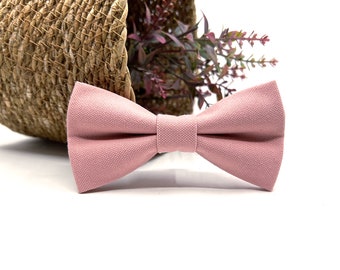 May include: A pink bow tie made of fabric. The bow tie is tied and ready to wear.