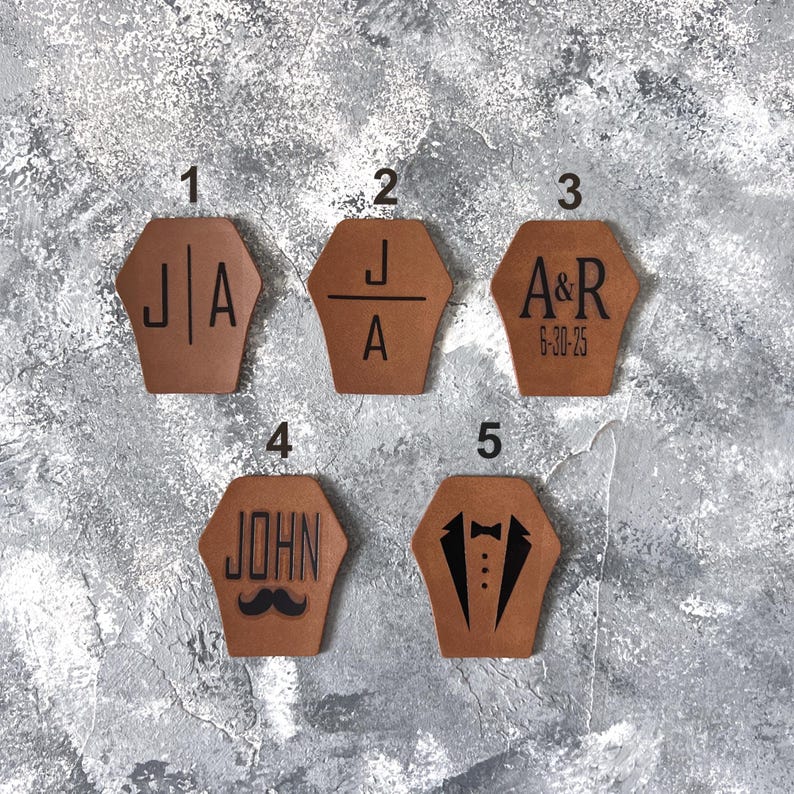 Op de afbeelding: Vijf bruine leren patches met verschillende ontwerpen. Patch 1 heeft de initialen "J|A". Patch 2 heeft de initialen "J/A". Patch 3 heeft de initialen "A&R" en de datum "6-30-25". Patch 4 heeft de naam "JOHN" en een snor. Patch 5 heeft een smoking met een strikje.
