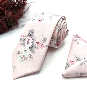 May include: A pink floral patterned tie and pocket square set. The tie has a pointed end and the pocket square is a triangle shape.