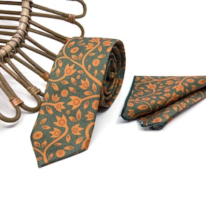 May include: A green and orange patterned tie and pocket square set. The tie features a floral design with orange flowers and green leaves. The pocket square has the same pattern.