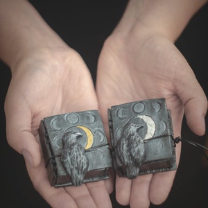 May include: Two small black leather-bound journals with silver and gold crescent moons and ravens on the covers.