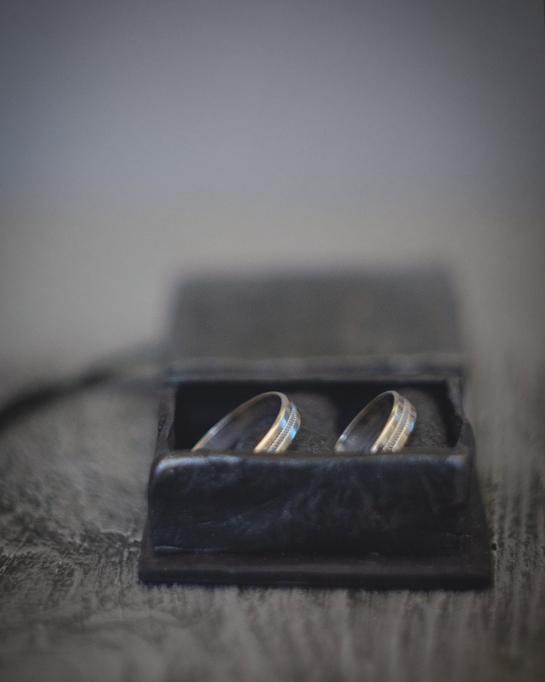 May include: Two silver wedding bands in a black velvet ring box.