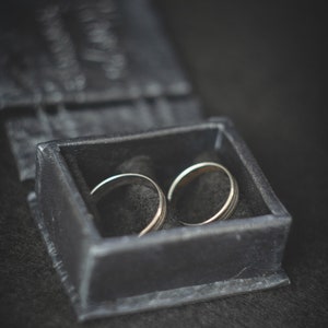 May include: Two silver wedding bands in a black velvet ring box.