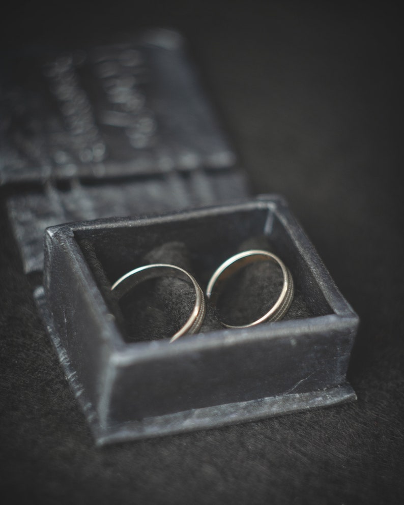 May include: Two silver wedding bands in a black velvet ring box.