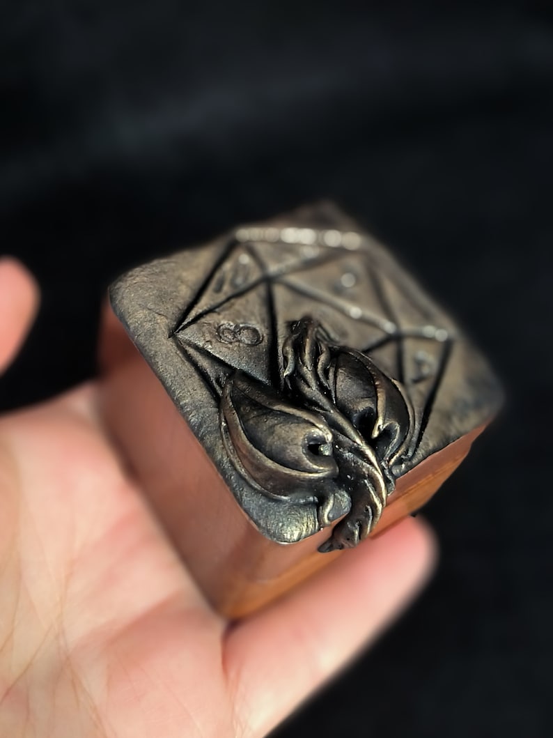 May include: A small wooden box with a metal design of a 20-sided die and a stylised leaf on the top.
