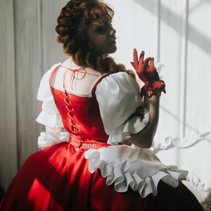 May include: A woman in a red and white dress with a white lace collar and a red ribbon tied at the back. She is wearing red gloves and has her hair in a braid.
