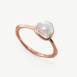 Puede incluir: Anillo de oro rosa con una gema clara grande de forma irregular. La gema está engastada en un bisel y la banda es de diseño simple y pulido. El anillo se muestra sobre un fondo blanco.
