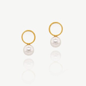 May include: A pair of gold earrings with a circle design and a pearl drop. The circles are textured and the pearls are white.