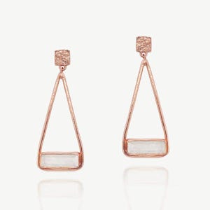 May include: A pair of rose gold earrings with a geometric design. Each earring features a textured square stud, a triangular frame, and a rectangular, light-coloured stone at the base. The earrings are displayed against a white background.